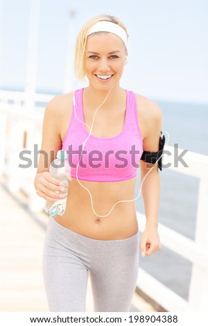 Young fit woman with water in pink sports bra on the pier over sea