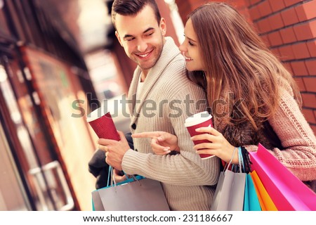 A picture of a joyful couple window shopping in the mall with coffee