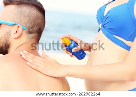 A picture of a woman applying sunscreen on the back of her man at the beach