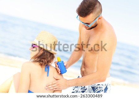 A picture of a man applying sunscreen on the back of his woman at the beach
