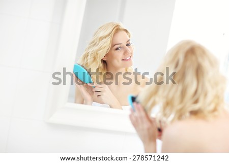 A picture of a happy woman brushing her hair in the bathroom