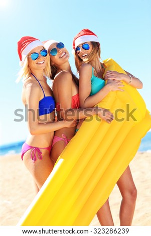A picture of a group of women in bikini and Santa's hats holding mattress on the beach