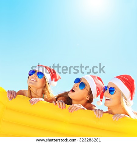 A picture of a group of women in bikini and Santa\'s hats holding mattress on the beach