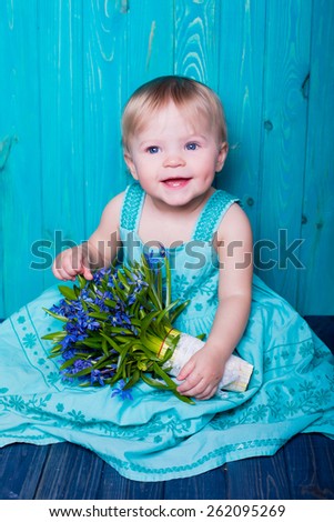 smiling emotional baby portrait summer style with bouquet of spring blue flowers on blue wooden background. present for holidays mother woman day easter