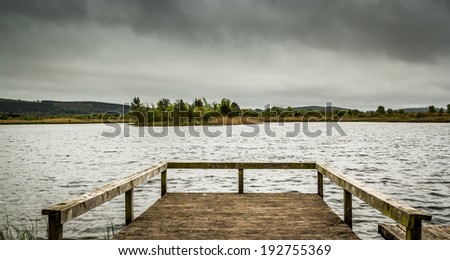 Lonely dock looking out onto lake with grey clouds above