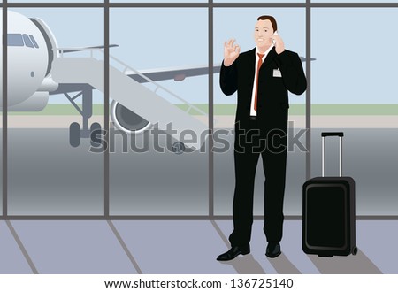 Success busy smiling businessman uses  his time while waiting between flights, he stays in the airport and shows sign ok with his hand and holds smart phone with the other hand