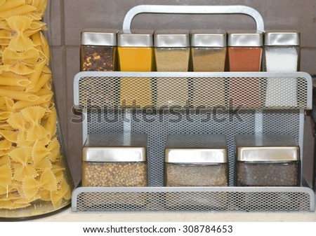 Small glass jars with spices and other kitchen condiments on a kitchen shelf