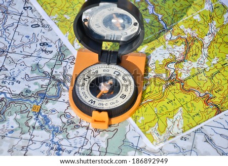 Open magnetic compass with mirror cover is lying on a topographic map.