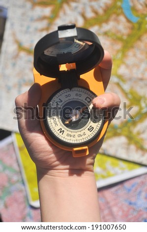 Open compass mirror cover in the palm of a man lying on the background of topographic maps.