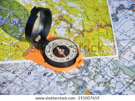 Open magnetic compass with mirror cover is lying on a topographic map.