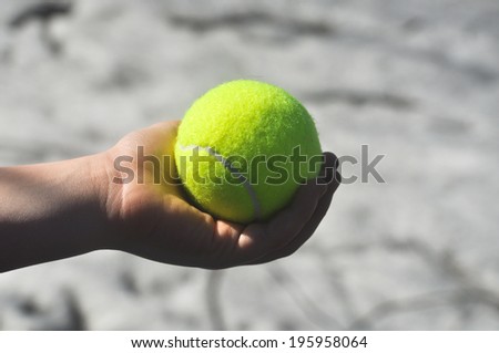 Tennis ball in his hand. The hand of the child squeezes yellow-green tennis ball against a light background.