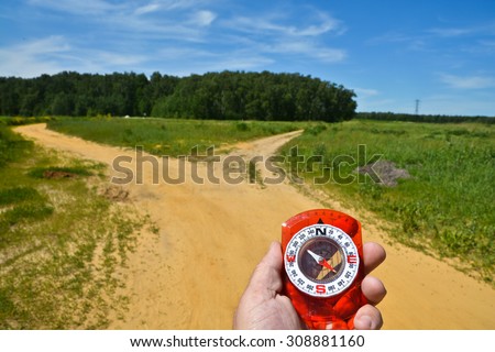 With the compass before the fork. The magnetic compass in the hand of a man to a fork in the road.