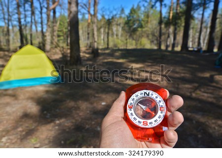 Compass and tourist tent. The magnetic compass in the hand against the tent in the forest in spring.