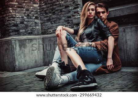 Young and trendy man and woman sitting on the street with brick walls. Fashion style