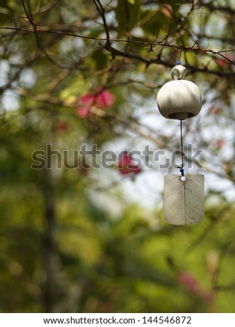 pearl white ceramic bell with elephant figure and sway leaf hanging in a garden