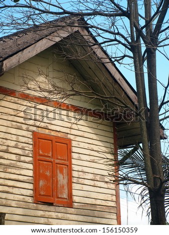 wooden house white country house with red brown window and a tree without leafs