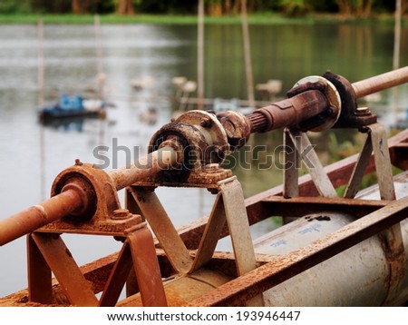 close up of a metal steel drive shaft of a water pump on a large size ball bearing support and universal joint with dark dirty grease with shrimp farm water surface in the background.
