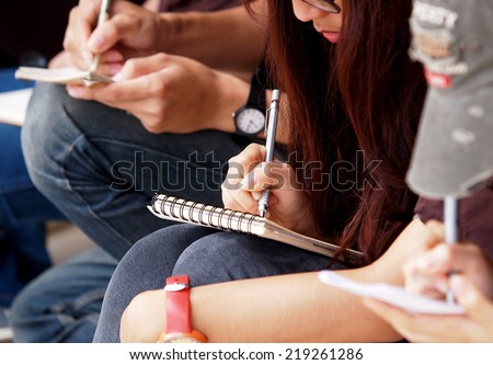 unidentified young asian female student school girls wearing jeans sitting on the floor outdoor taking note at site visit on small paper notebook with pen and pencil