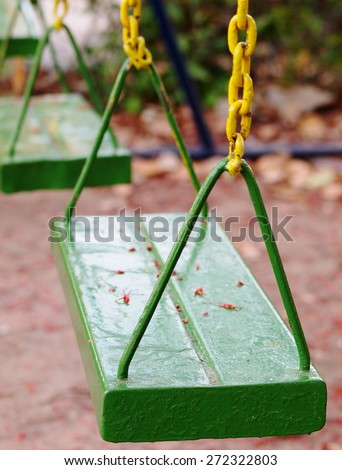metal swing for children on outdoor playground in a kindergarten made of iron plate chain and rod painted in colorful green color hanging outdoor in backyard garden under evening sunlight and shadow