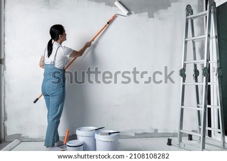 girl paints a white wall with a roller. Repair of the interior. Young female decorator painting a wall in the empty room, concept builder or painter in helmet with paint roller over the empty room. Foto d'archivio © 