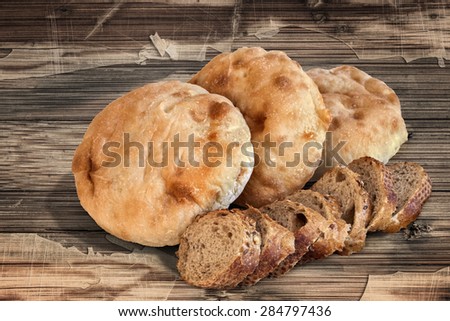 Three Pita Bread loafs and Baguette Integral Brown Bread slices, on old, weathered, Wooden Table surface.