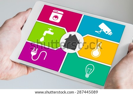 Smart home automation and mobile computing concept. Hands holding modern white and silver tablet with home automation dashboard screen.