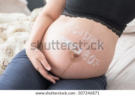 pregnant woman with painted on white paints cream - loading 80%, looking forward to long awaited child