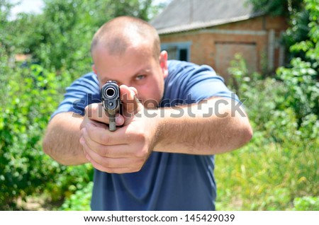 man with a pistol in hands on buildings and of bushes