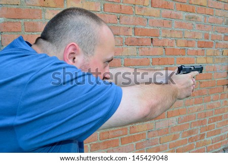 a man with a pistol in hands on a brick wall