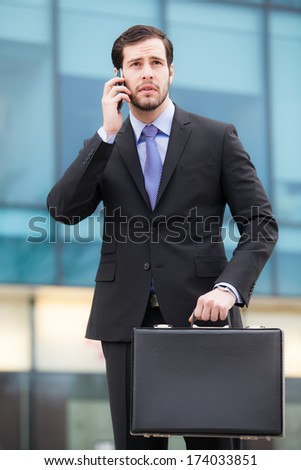 businessman talking on the phone in front of an office building with a briefcase in hand