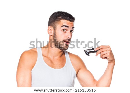 young handsome man in white shirt trimming his beard with a trimmer