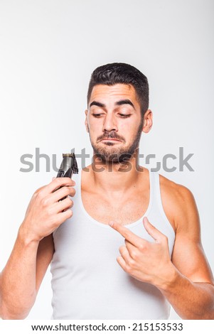 young handsome man in white shirt trimming his beard with a trimmer