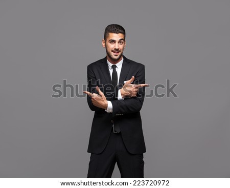 handsome hispanic elegant man in black suit on grey background, pointing directions