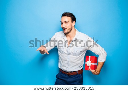 handsome man hiding a christmas gift behind him on blue background