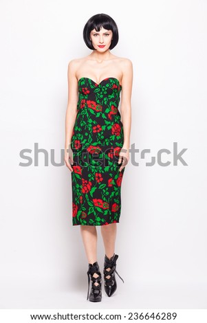 young brunette woman posing in modern dress with red and green flowers and wearing high heels