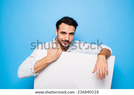 smiling handsome man looking into camera and holding a blank panel on blue background