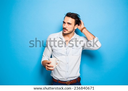 handsome man thinking on something and scratching his head, holding a cup of coffee in hands