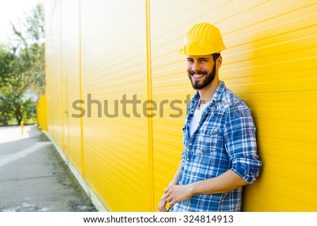 worker with helmet and yellow plaid shirt near a wall