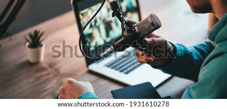 A man host streaming his audio podcast using microphone and laptop at his small broadcast studio, close-up