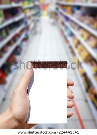white blank vertical notebook in woman hand and supermarket background
