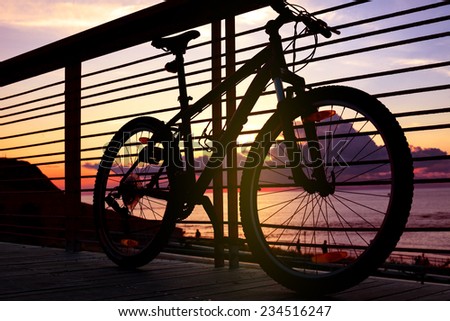 silhouette of mountain bike near the railing in front of the ocean at sunset