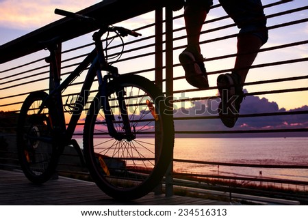 silhouette of young and active sportsman and his mountain bike sitting on the railing near the ocean