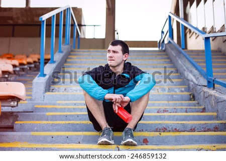 tired sportsman sitting on the stairs with red plastic sport bottle with water