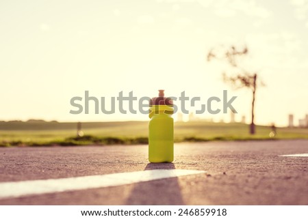 plastic sport flask with water and minerals on the road in park at sunset