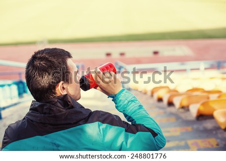 tired sportsman drinking water at stadium