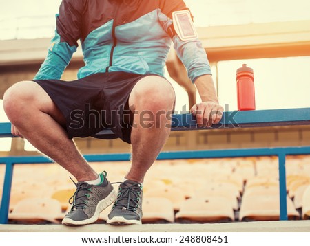sportsman with a bottle of water sitting and resting at the railing at the stadium