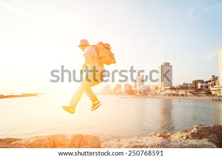 brave man jumping over rocks near sea and city on the background