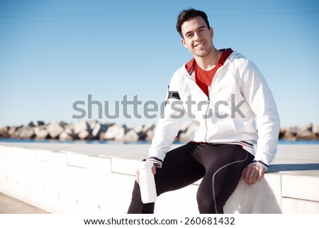 smiling male athlete with bottle of water relaxing after workout outdoors