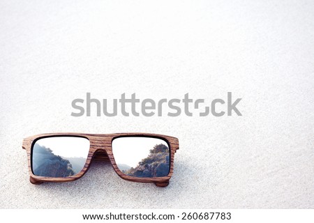 double exposure of wooden sunglasses and mountains with white sand background