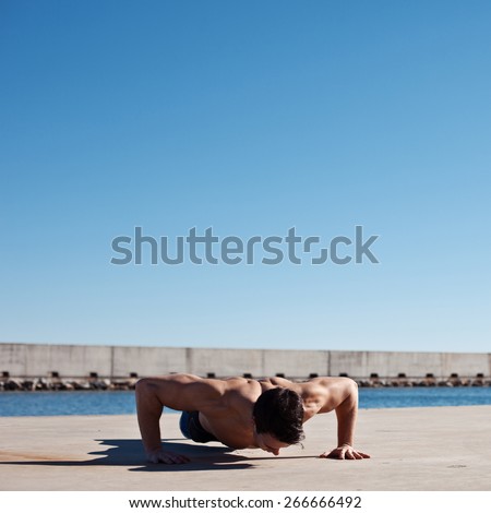Strong and muscular athlete with naked torso doing push-ups outdoors